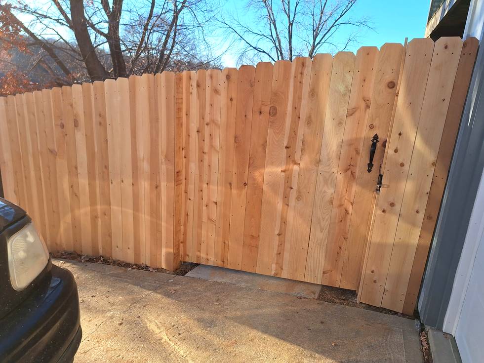 A cedar privacy gate with a slim ornate black pull and thumb latch mounted on the face of the boards.