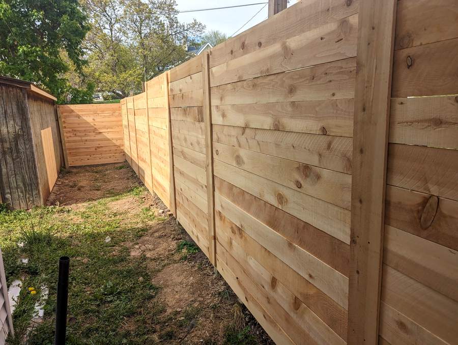 A horizontal cedar plank fence turning a corner where it meets an older weathered fence.