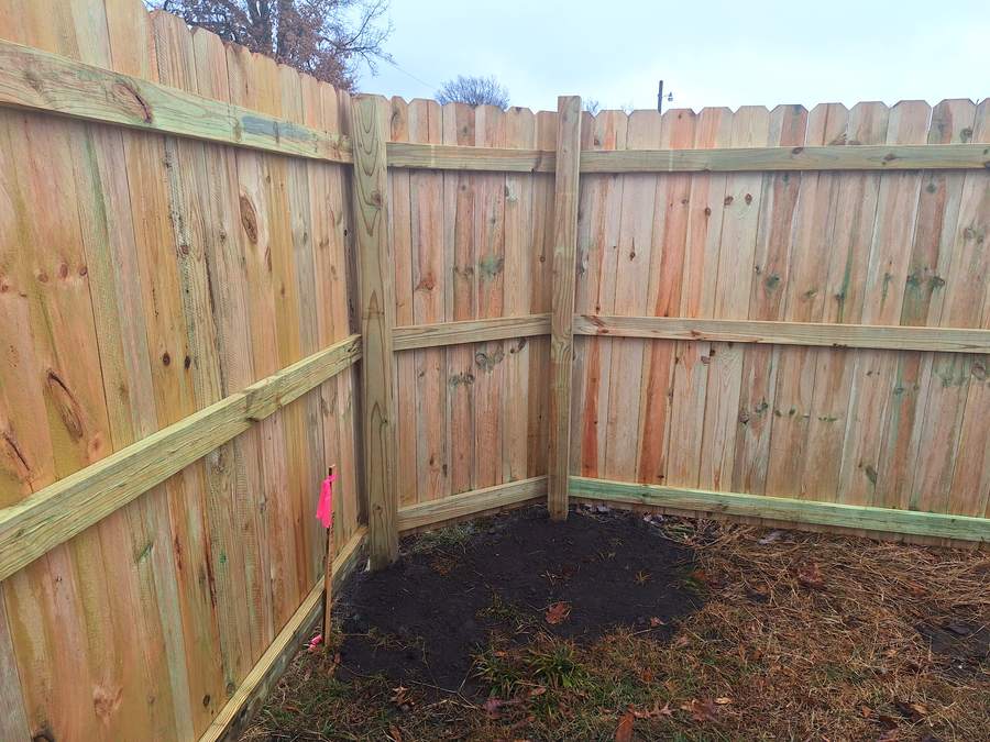 Two runs of solid cedar privacy fence meeting at a corner post over freshly turned dirt.