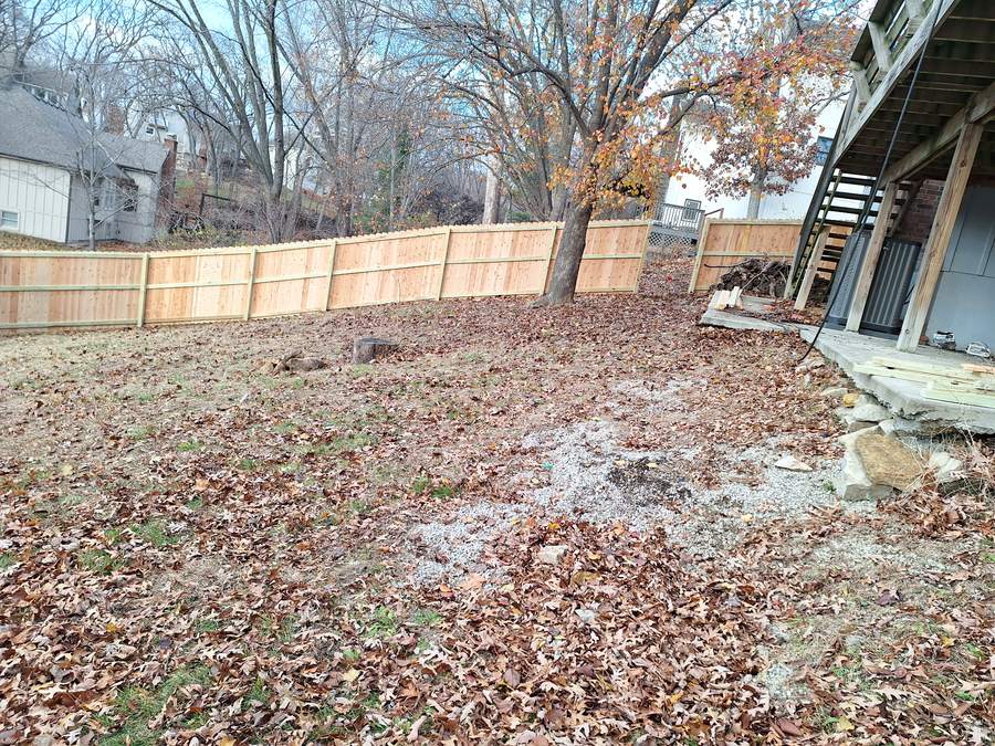 A solid cedar privacy fence running across the back of a leaf-covered yard below a raised deck.