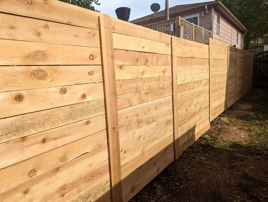 A modern horizontal cedar plank fence, wide boards run side to side between posts along a driveway.